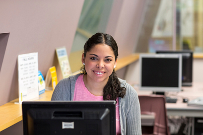 A young female student is sitting at one of several available public computers